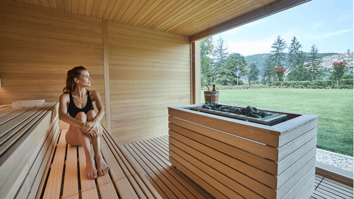 Woman relaxing in a sauna while looking out a large window at nature