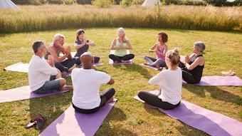Group Of Mature Men And Women In Class At Outdoor Yoga Retreat Sitting Circle Meditating