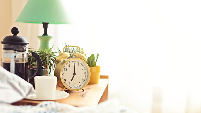 Alarm clock and coffee cup at bed in sunny room