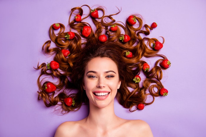 smiling woman with clear skin surrounded by strawberries