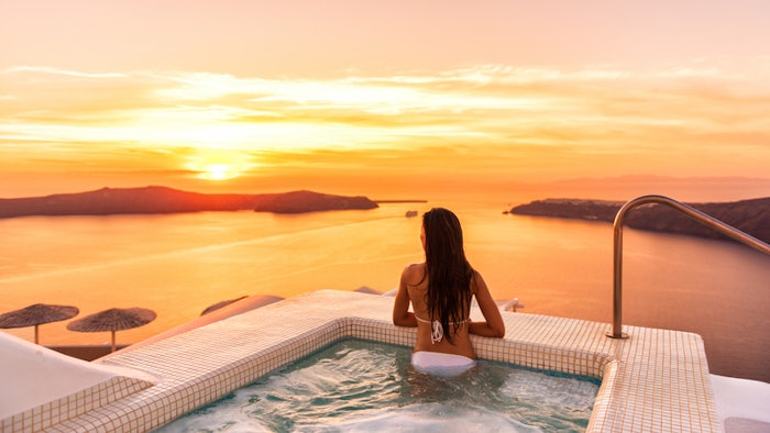 Luxury travel Santorini vacation woman swimming in hotel jacuzzi pool watching sunset