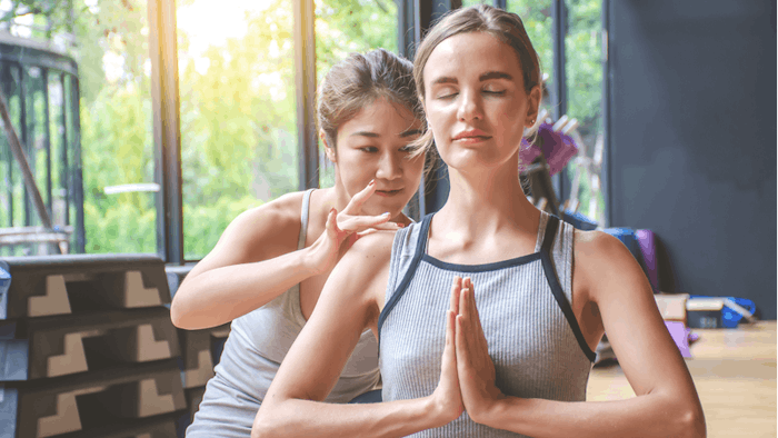 yoga teacher with student working out in sports club, instructor helping female student with positioning on her yoga pose in class