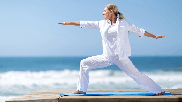 senior woman doing yoga on the beach - wellness trend