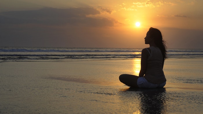 Silhouette of young beautiful asian woman meditating on sand water free and relaxed looking at the sun on sunset beach