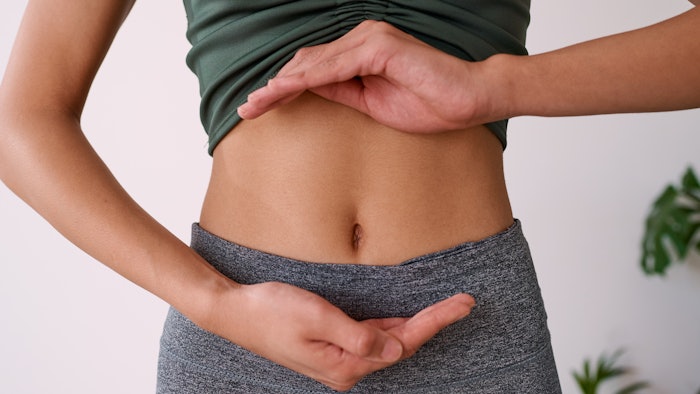 Close up of a young multi-ethnic woman's stomach cupped by her hands, gut health
