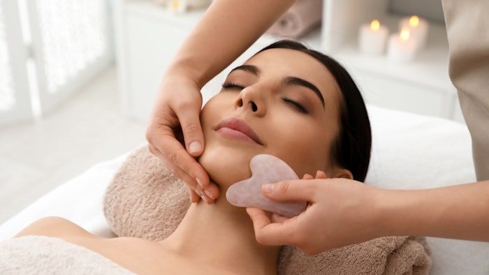 woman receiving facial massage with gua sha tool in wellness spa