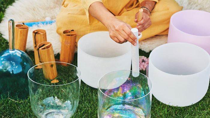 Woman playing music on crystal singing bowls, relaxing in beautiful green garden