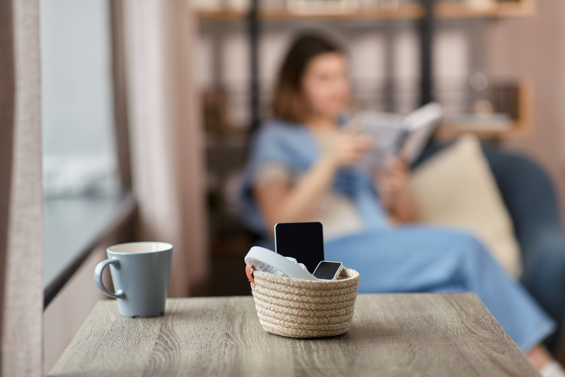digital detox and leisure concept - close up of gadgets in basket on table and woman reading book