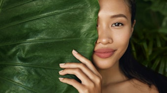 Beauty face. Woman model with natural makeup behind green leaf