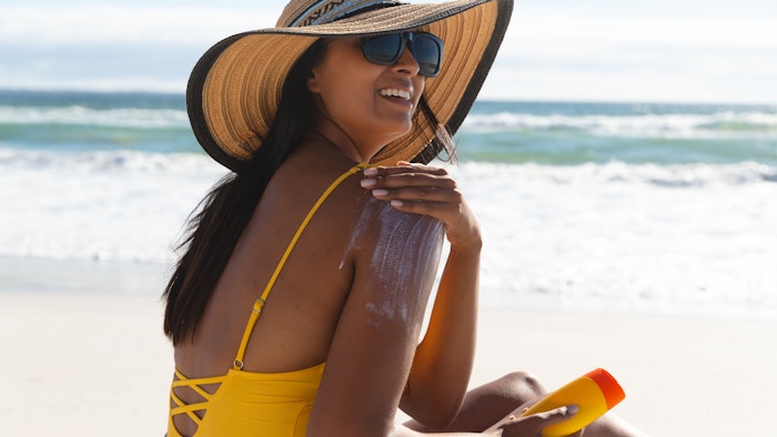 mixed race woman applying sunscreen on beach