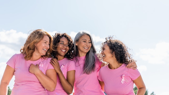 Cheerful multiethnic women with ribbons of breast cancer awareness hugging outdoors
