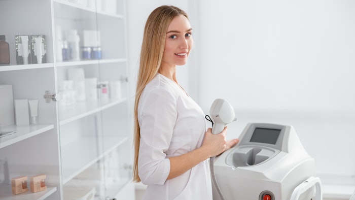 Young woman using laser epilation machine in beauty salon