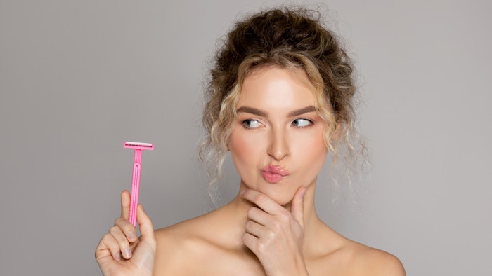Portrait of young beautiful thoughtful lady looking at safety razor and touching chin,