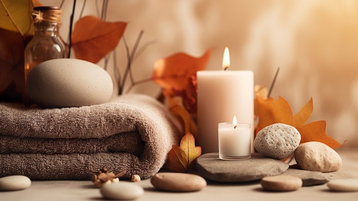 Autumn spa scene with candles, stones and towel, in earthy tones.