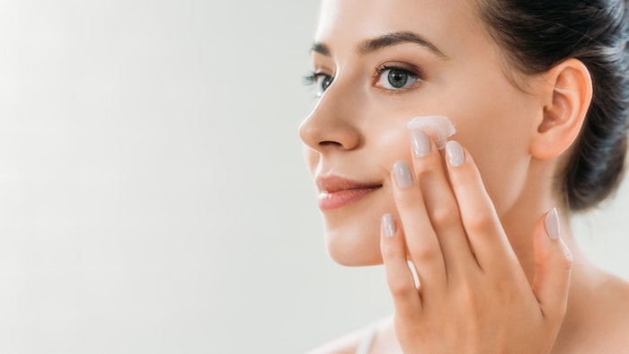 beautiful smiling young woman applying face cream and looking away