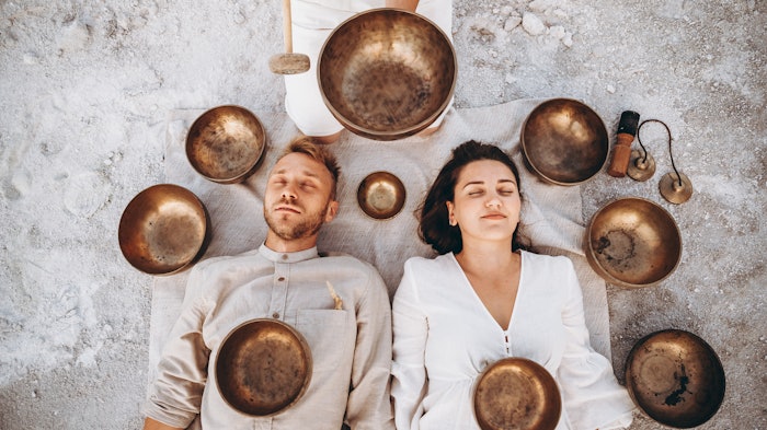 group therapy with Tibetan singing bowls for a girl and a boy lying on the ground in the middle of the desert surrounded by copper bowls, meditation and relaxation