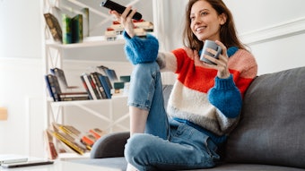 Photo of girl drinking coffee and using remote control while watching tv