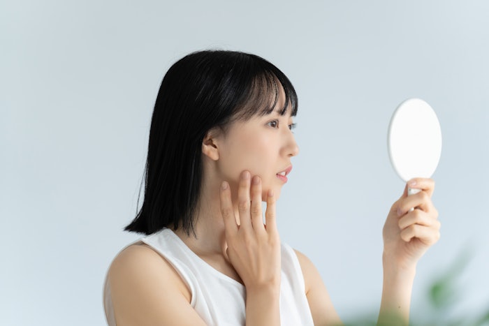asian woman looking at acne in mirror