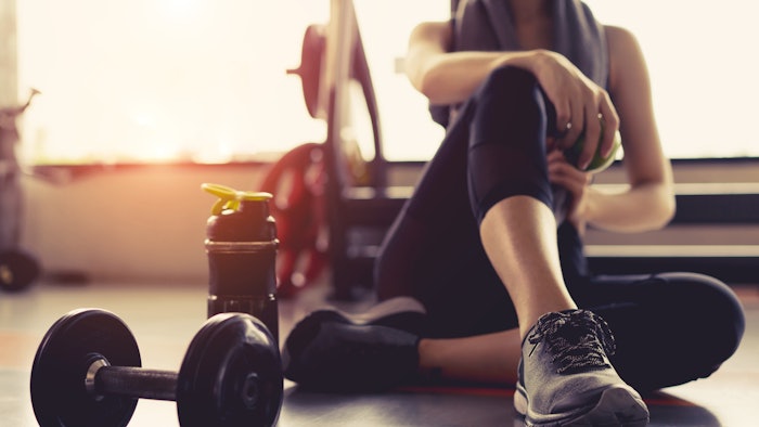 Woman exercise workout in gym fitness breaking relax holding apple fruit after training sport with dumbbell and protein shake bottle healthy lifestyl