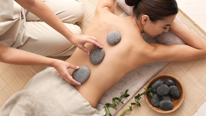 Beautiful young woman getting hot stone massage in spa salon, top view