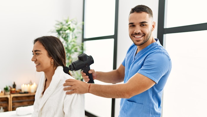 Latin man and woman wearing physiotherapy uniform massaging neck using percussion gun at beauty center