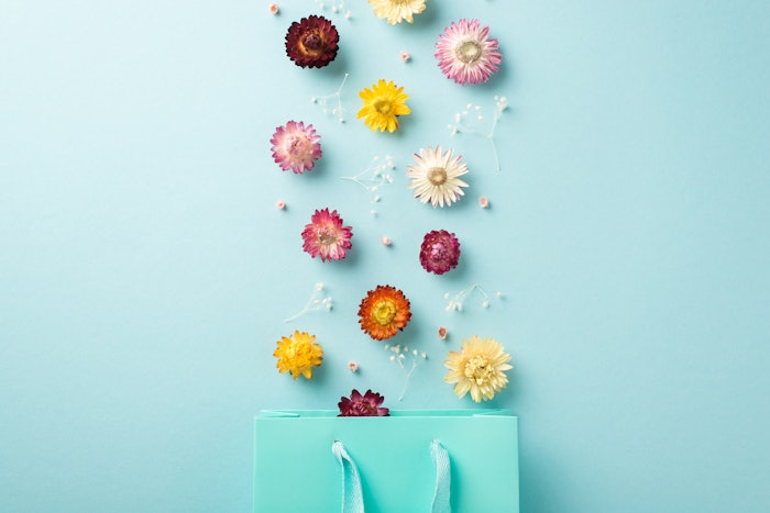 Top view photo of woman's day composition blast of wild flowers from blue present bag on isolated pastel blue background, spa products spring concept