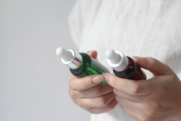 Female hands holding two bottles of facial essential oil or serum packaging. Woman choosing beauty products.