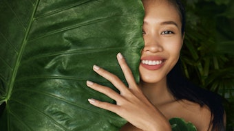 Beauty face. Woman model with natural makeup behind green leaf