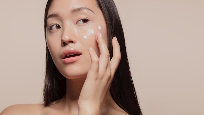 Asian woman applying moisturizer to her face