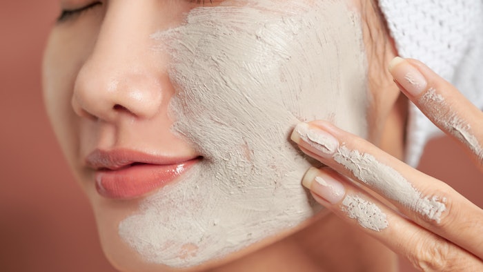 Close-up portrait of attractive girl with a towel on head and clay mask on face isolated over orange background.