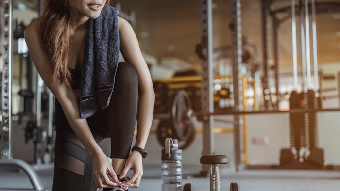 fitness, workout, gym exercise, lifestyle and healthy concept. Women are using their hands to tie their shoes, have a dumbbell and a bottle of water beside them. Prepare for exercise in the gym