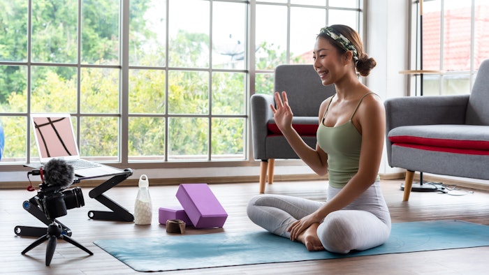 Young yoga master recording video content for her online course with camera and laptop