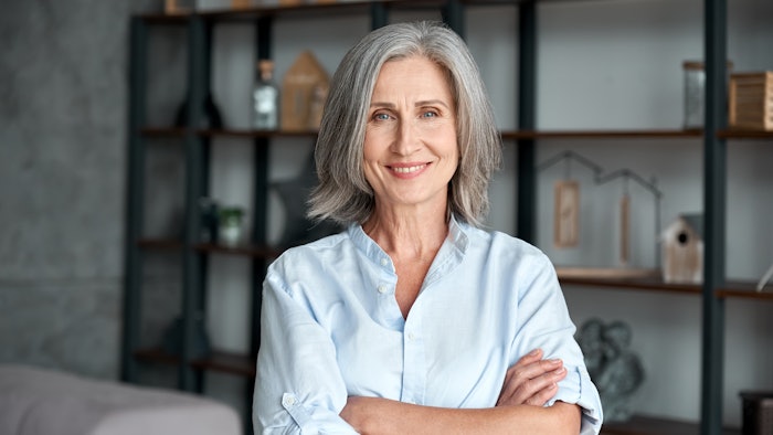 Smiling confident stylish mature middle aged woman standing at home office.