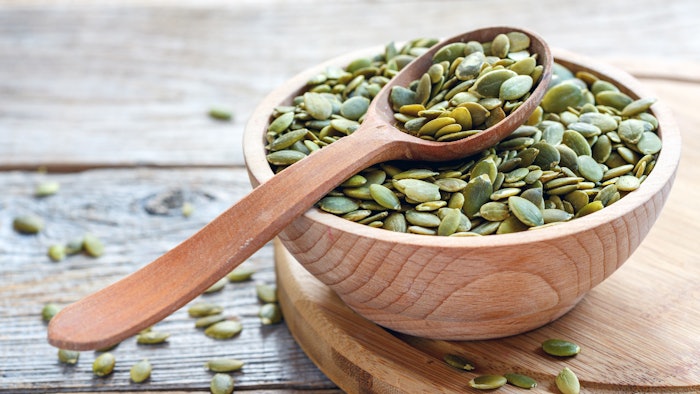 Wooden bowl of pumpkin seeds and a spoon.