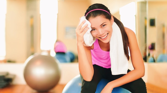 Asian fitness girl training at gym wiping sweat with towel post workout happy in gym background.