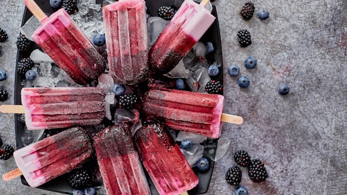 Homemade fresh frozen blueberry and blackberry popsicles on black plate with ice sitting on stone