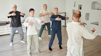 Wide shot of senior people meditating during qigong exercise in fitness studio while male instructor teaching