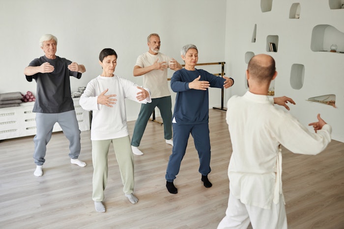 Wide shot of senior people meditating during qigong exercise in fitness studio while male instructor teaching