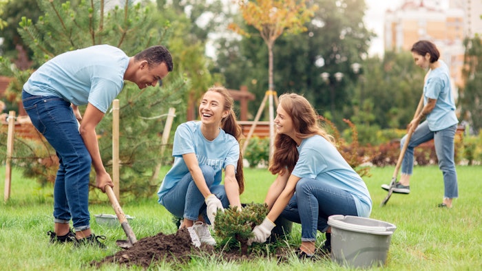 Volunteering. Young people volunteers outdoors planting trees digging ground talking cheerful