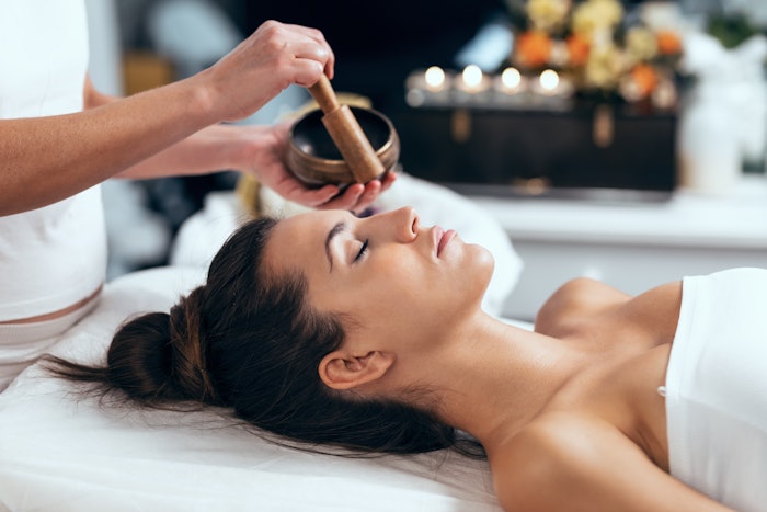 Beautiful young woman having sound healing holistic treatment in health spa center