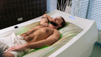 Confident young man with beard lying relaxing on electric massage bed and enjoying spa treatment at luxury spa. Muscular male having rest and enjoying automated wellness treatment.