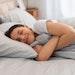 Content woman hugging blanket and smiling in bed
