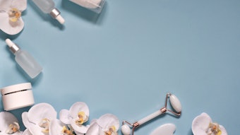 Beauty Products. Facial Roller, essential oils, cream of skincare and beautiful orchids on blue background. Flat lay, top view with copy space. Massage tool for facial skin care, SPA beauty treatment