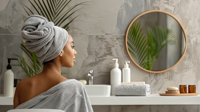 Experience the serene ambiance of a modern minimalist bathroom, where a woman in a gray towel indulges in self-care