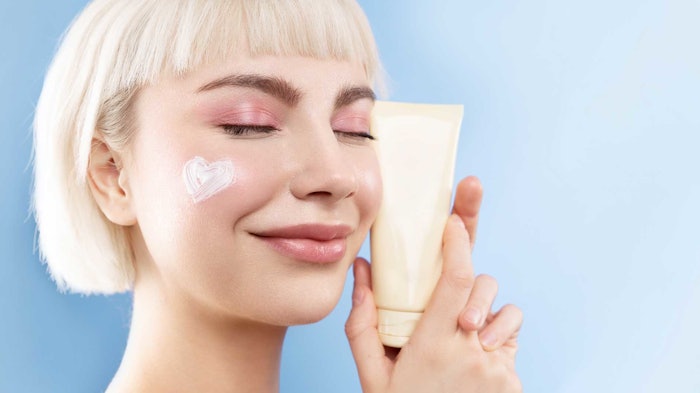 happy platinum blonde woman shiny skin holding product tube near and dear to her face