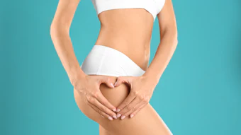 Closeup view of slim woman in underwear making heart with hands near thigh on color background. Cellulite problem concept