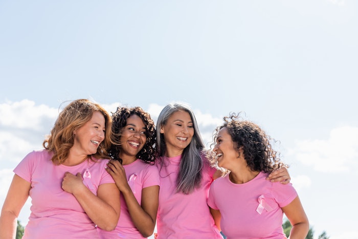 Cheerful multiethnic women with ribbons of breast cancer awareness hugging outdoors