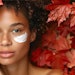 Model with flawless skin applying skincare in an autumn leaves setting for Fall