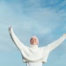 Portrait of happy young woman with cancer with arms up