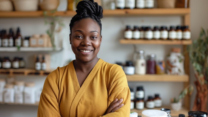 Smiling woman in yellow outfit standing in a natural products store, surrounded by shelves of organic goods and cosmetics..